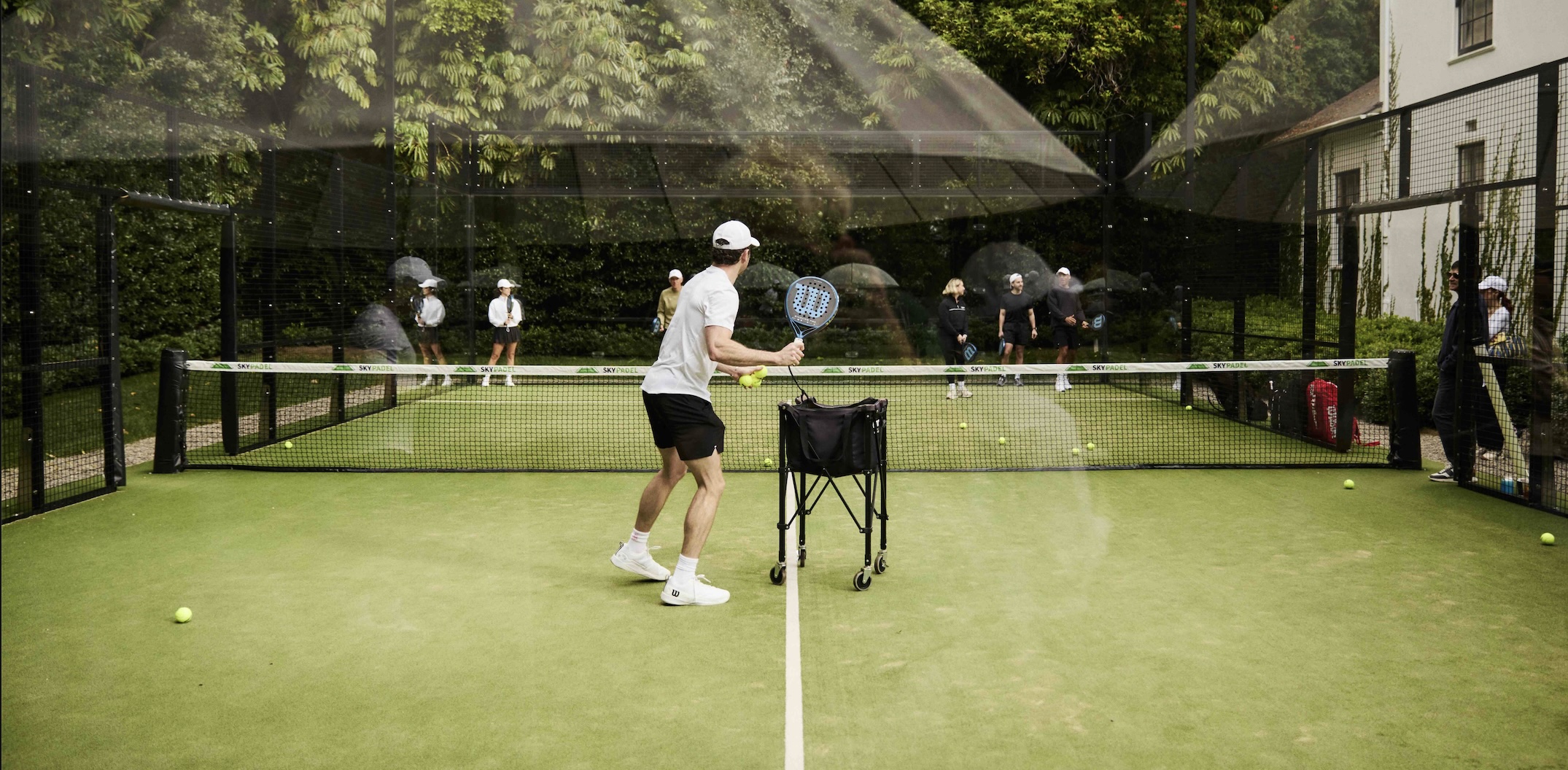 People playing padel on an outdoor court with a coach and practice balls