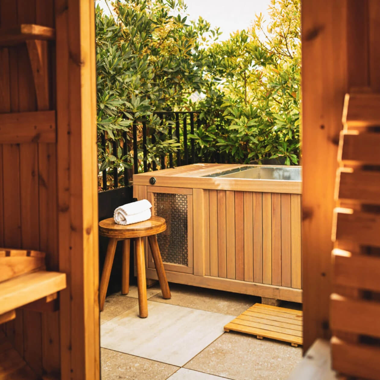 Private outdoor cold plunge tub beside cedar sauna surrounded by lush greenery at luxury wellness retreat