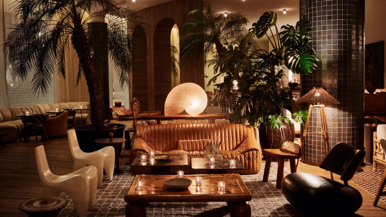Indoor lounge with seating, wooden coffee table, large plants, and soft ambient lighting