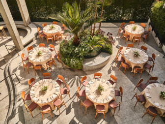 Open-air dining space with multiple round tables, chairs, and a central planter with greenery