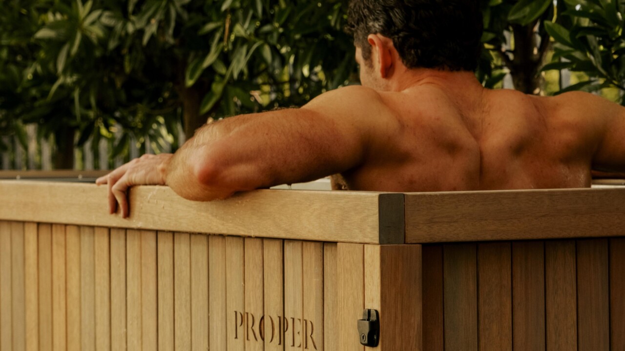 Man relaxing in a wooden outdoor soaking tub surrounded by greenery