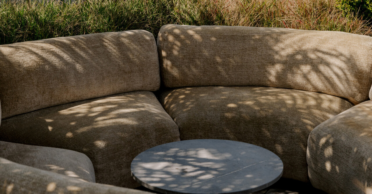 Cozy outdoor lounge seating with soft shadows, curved sofa design, and relaxed resort ambiance surrounded by natural greenery