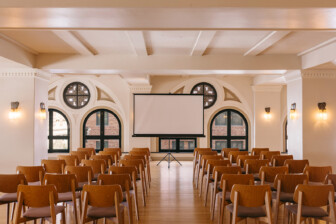 Elegant event and presentation space with arched windows, warm lighting, and refined conference-style seating arrangement