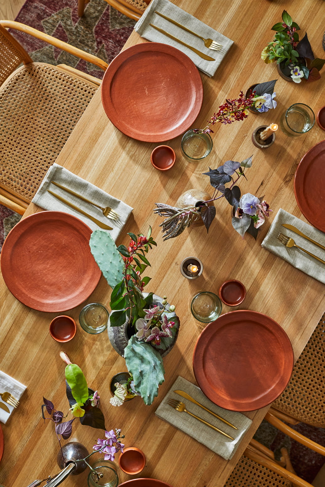 Wood dining table set with ceramic plates, gold flatware, and floral centerpieces