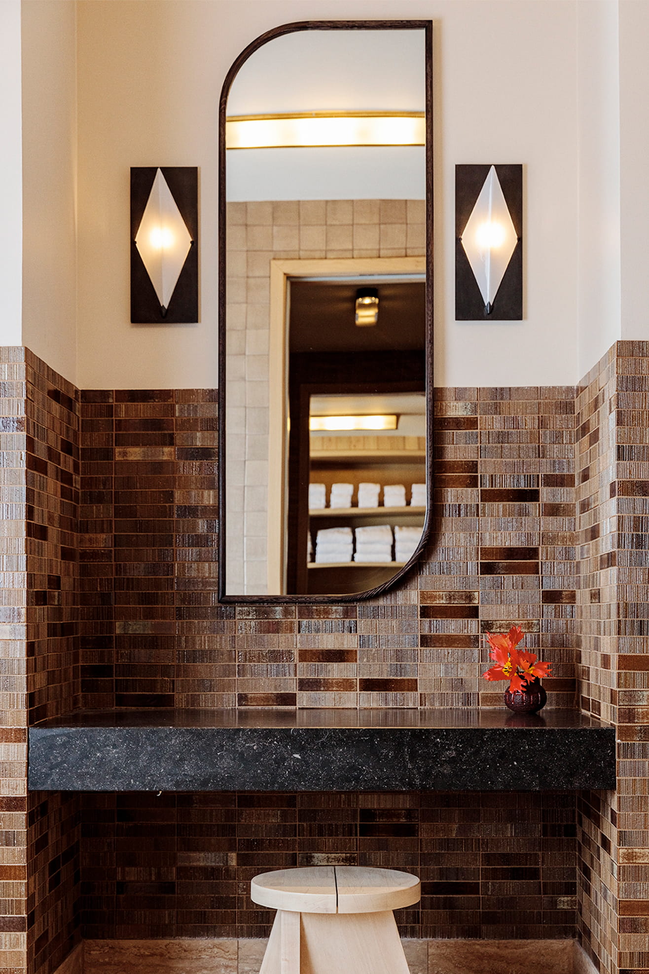 Spa vanity with arched mirror, warm wall sconces, and textured tile surround