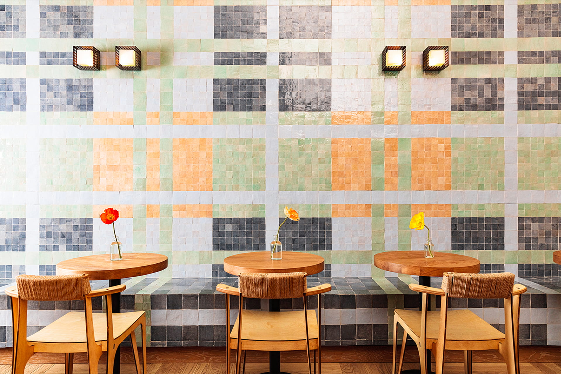 Café interior with wood tables, woven chairs, and pastel tile wall. Minimalist, warm, and colorfully inviting.