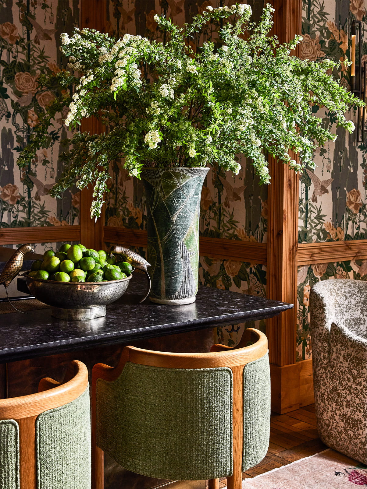 Decorative interior vignette with a vase of flowers and a bowl of limes on a marble counter against patterned wallpaper