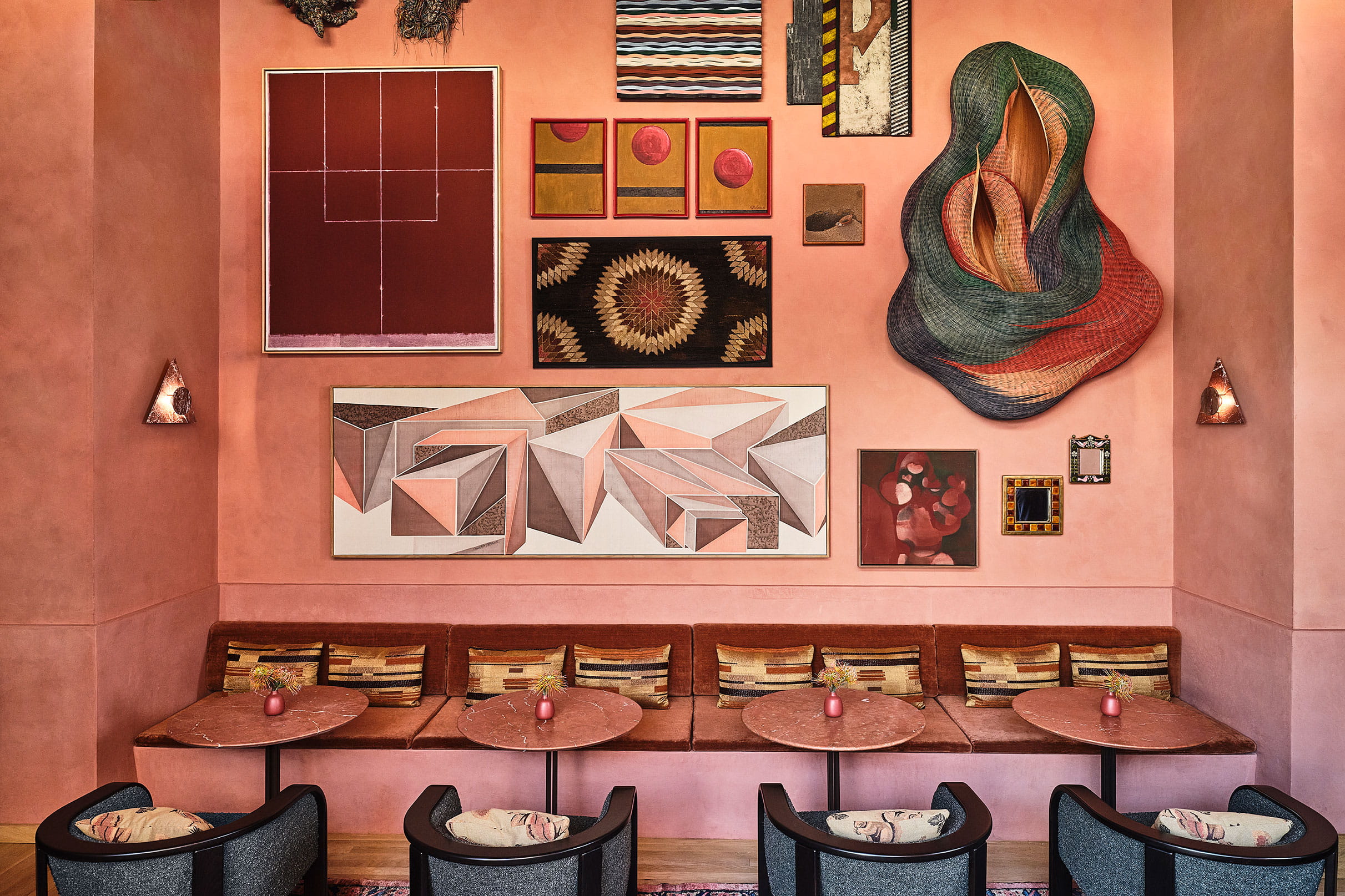 Stylish lounge with pink walls, built-in seating, marble tables, and a curated gallery wall of abstract art and textiles